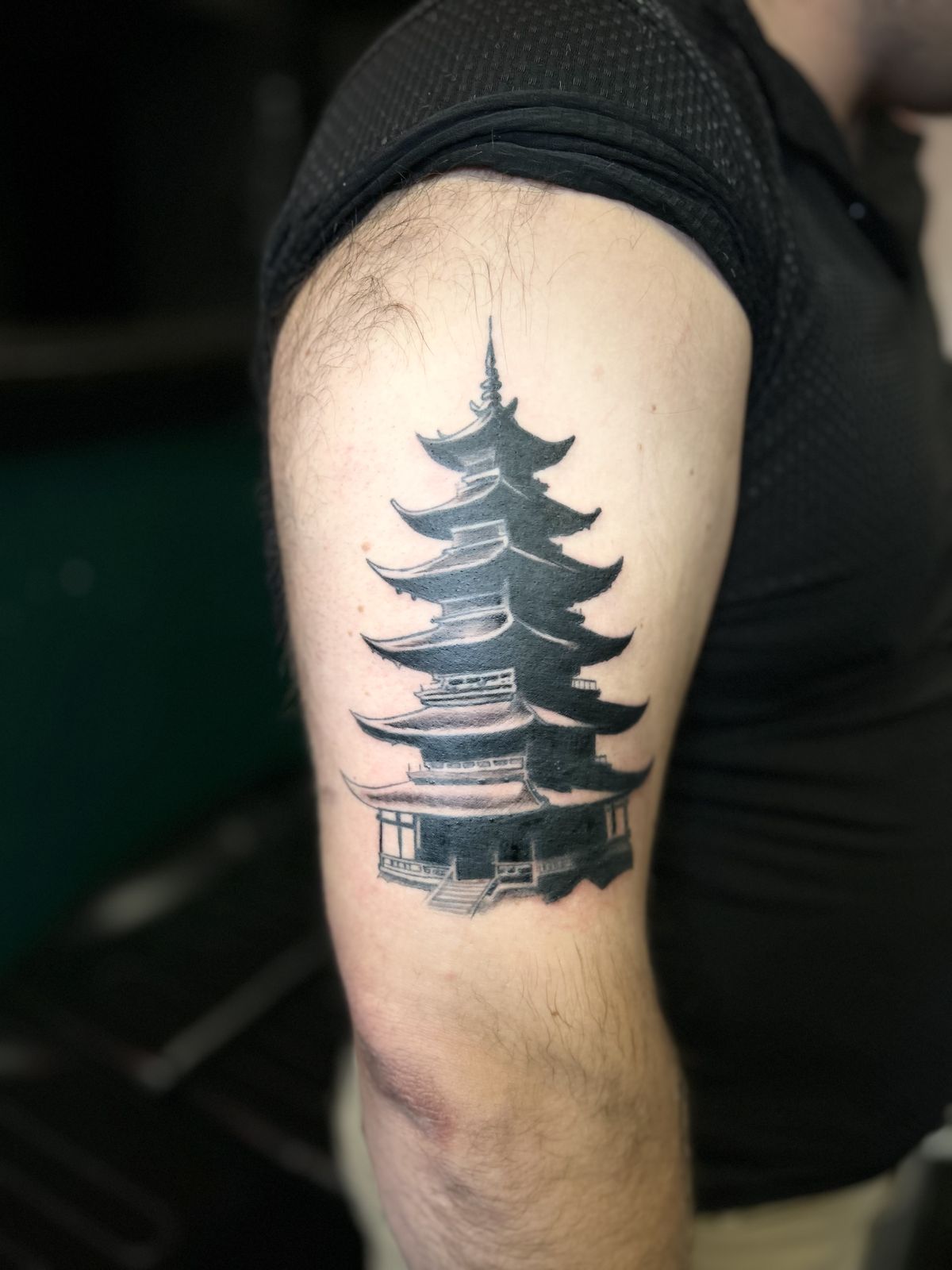 Black and grey pagoda tattoo on the upper arm