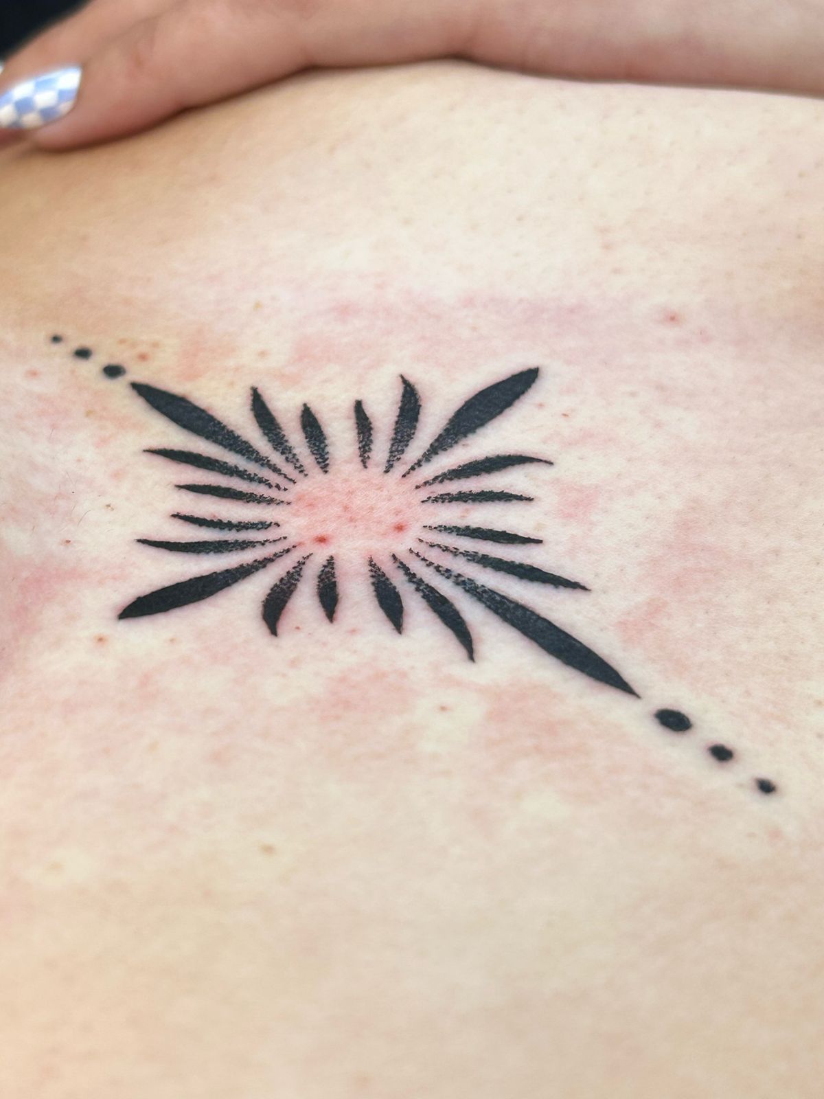 Blackwork sunburst tattoo on the sternum