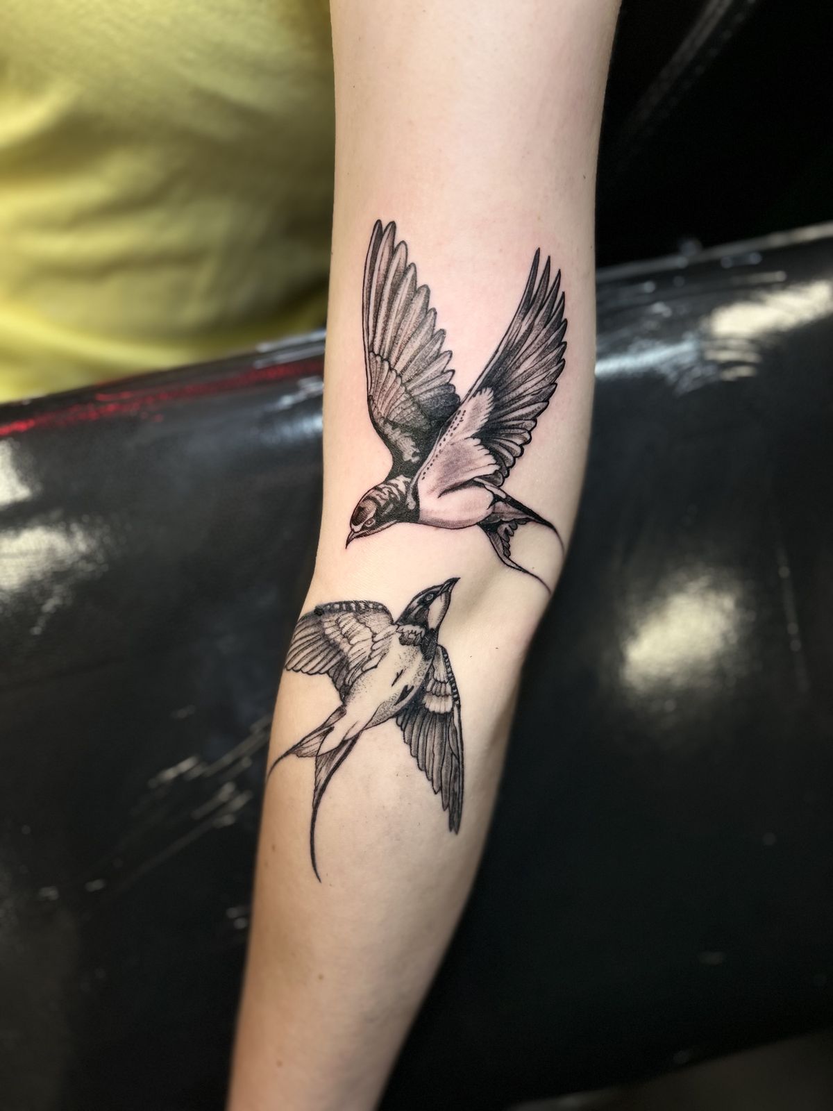 Two black and grey swallows tattooed on the forearm